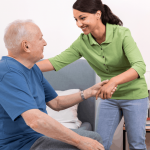 Woman providing home care byhelping an older man stand up from a seated position on a bed