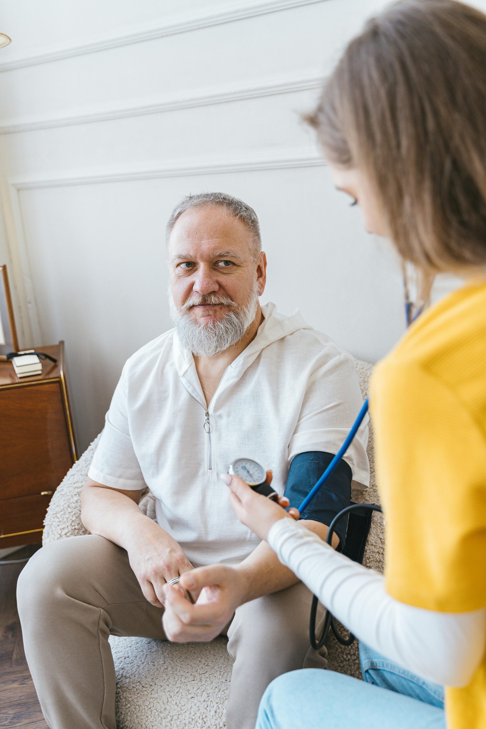 A healthcare worker takes the blood pressure of an elderly man using a monitor in a cozy indoor setting.